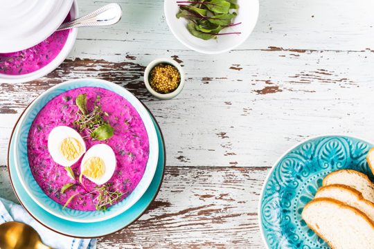 Cold soup made from beets cucumbers and garnished with an egg in a blue plate on a wooden background top view