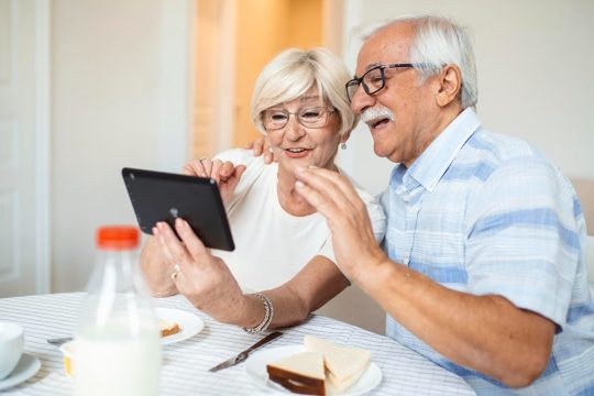 Senior man and his wife are using a digital tablet and communicating with their kids happy senior couple is having breakfast and having an online conversation with their family and sending greetings