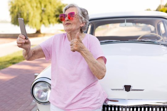 Happy senior woman standing next to her car