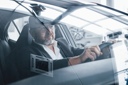 Bearded gentleman. reflection of the room in the front window of the car. senior businessman inside