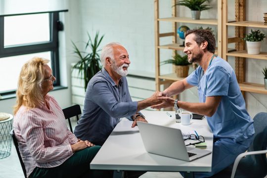 Happy male doctor shaking hands with senior man who came to medical appointment with his wife