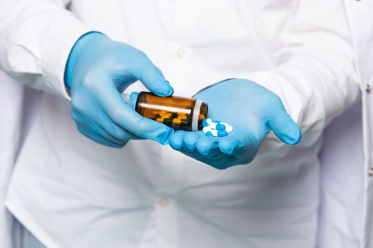 A front view man using pills in white shirt in blue gloves