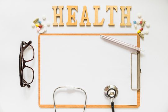 Health text with pills over the clipboard with paper; eyeglasses; pen and stethoscope