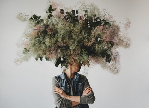 Large decorative bouquet made of green leaves and moss hangs over man's head