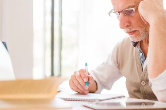 Senior professor in glasses writing on notebook in classroom