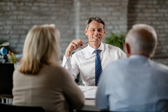 Happy financial advisor communicating with senior couple while having meeting with them in the office