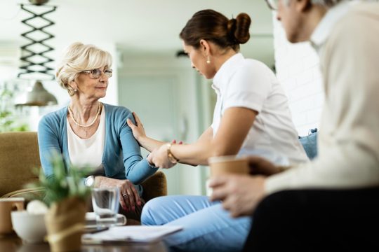 Female nurse communicating with senior woman while being in home visit focus is on senior woman
