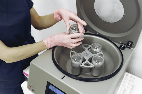 Crop unrecognizable cosmetologist taking test tube out of centrifuge for plasma in modern clinic