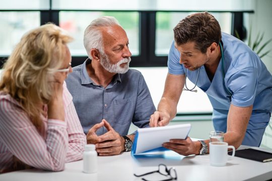 Serious doctor discussing with senior couple about their medical documents during appointment at clinic