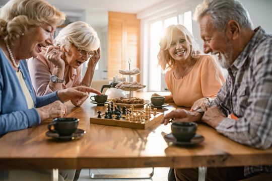 Group of happy seniors playing chess and having fun together at home