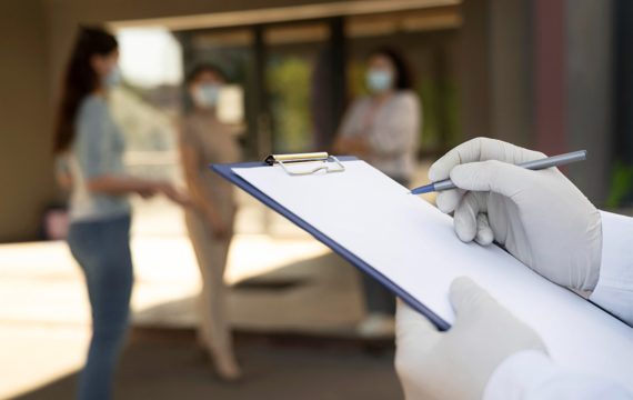 Doctor holding notepad at the vaccination center with patients outdoors