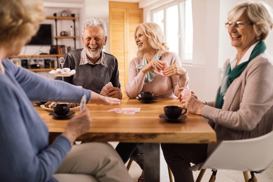Group of happy mature people laughing while enjoying in card game at the table