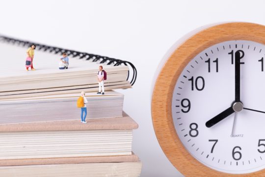 Closeup shot of little figurines of students standing on textbooks next to a clock