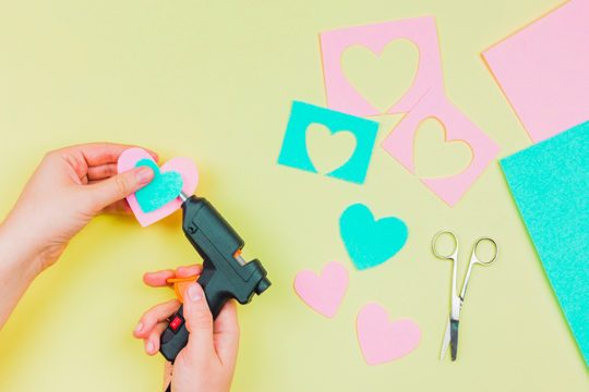 Close-up of woman's hand sticking the paper heart shape with electric hot glue gun