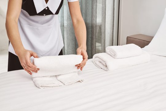 Cropped portrait of housecleaner rolling towels on bed while cleaning bedroom and preparing everything for clients to move in, making room look neat and tidy. maid on duty trying her best