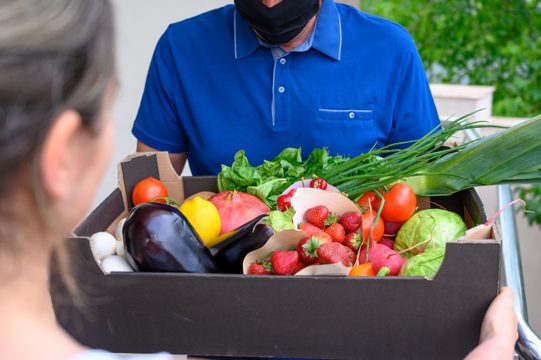 Delivery man wearing a face mask and holding a box with vegetables