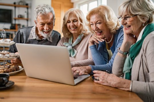 Happy senior friends enjoying while watching together something on laptop at home