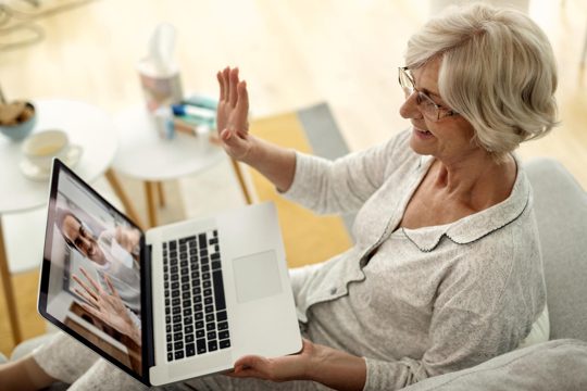 Happy senior woman waving while having video call with her son from home