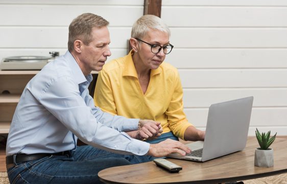 Senior man looking through his laptop next to his wife