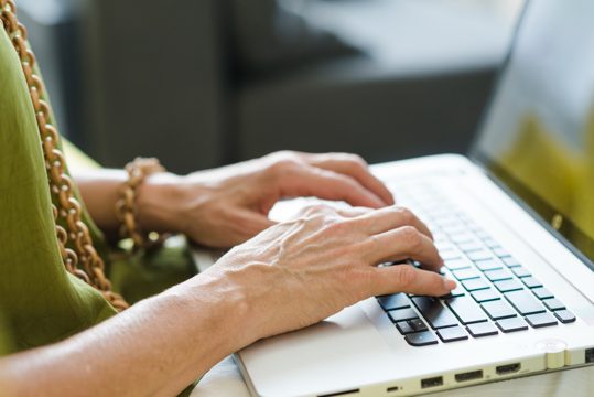 An aged woman's hand typing on laptop