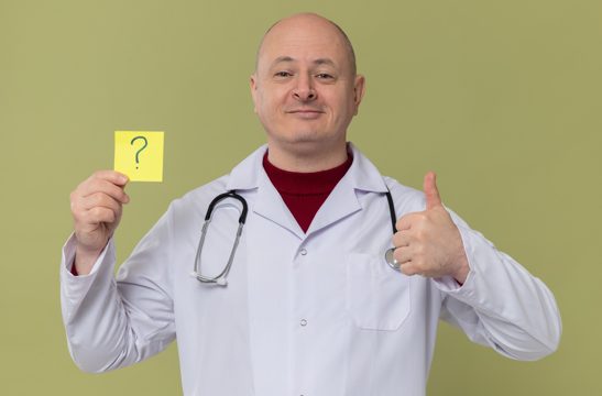 Pleased adult slavic man in doctor uniform with stethoscope holding question note and thumbing up