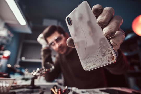 Electronic technician showing a modern smartphone with a broken body in a repair shop