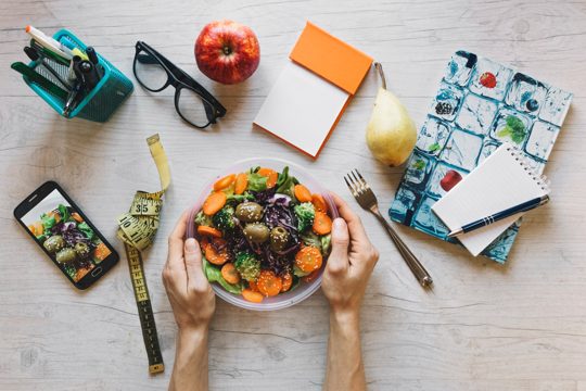 Crop hands holding bowl with salad in office