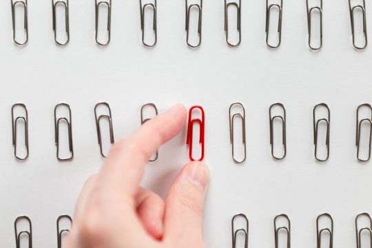 Hand picking among metal paperclips one red, different from others