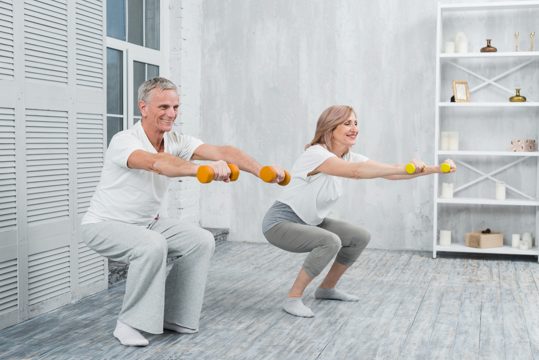 Smiling elder couple performing exercise with dumbbells at home