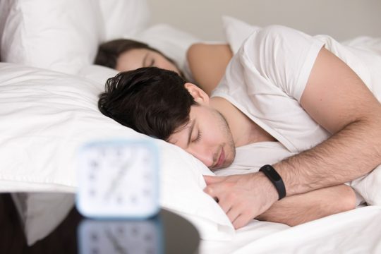 Couple lying asleep in bed, man wearing wristband smart watch