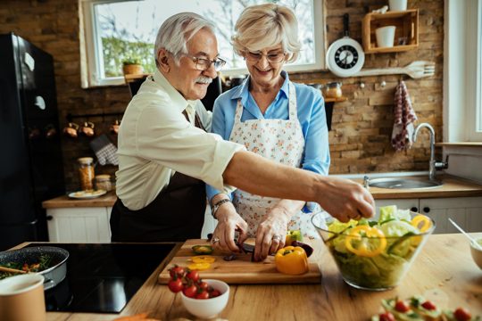 Happy mature couple making salad while preparing food together in the kitchen.