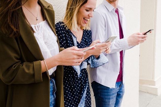 Group of happy friends standing outside looking at mobile phone