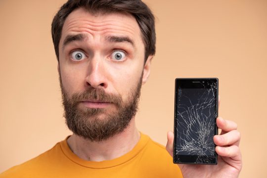 Portrait of a shocked young man showing his broken smartphone