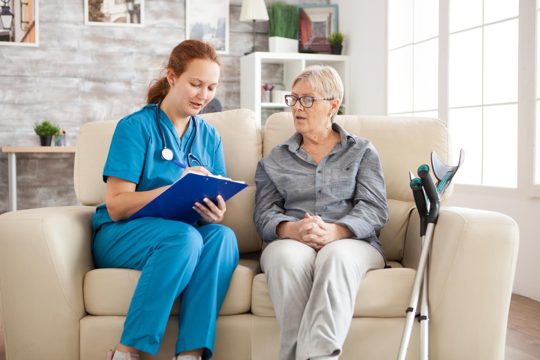 Female doctor in nursing home doing survey on senior woman with crutches