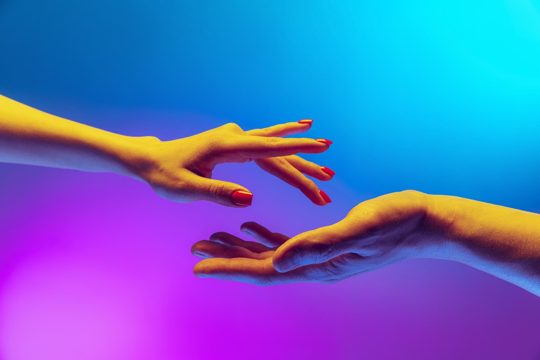 Tender touch studio shot of two hands reaching each ohter isolated over gradient blue purple background in neon