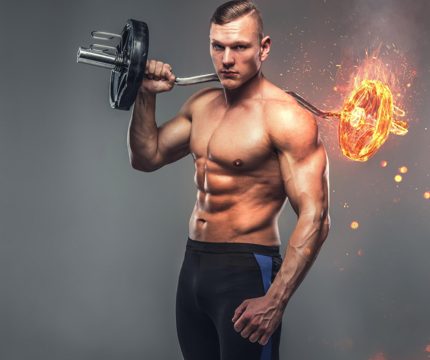 The shirtless muscular, athletic male holds the burning barbell on grey background.