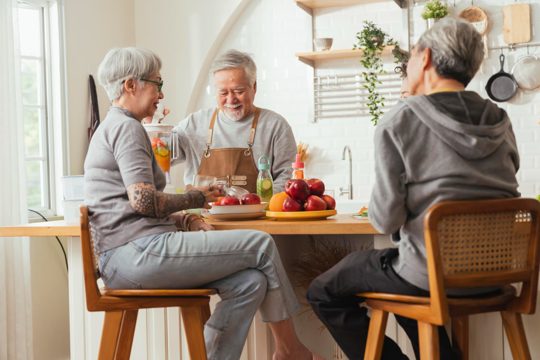 Group of senior friends having party indoors cooking and talking positive conversation in senior daycareasian senior male standing in kitchen and relaxing at home while eating a healthy food recipe