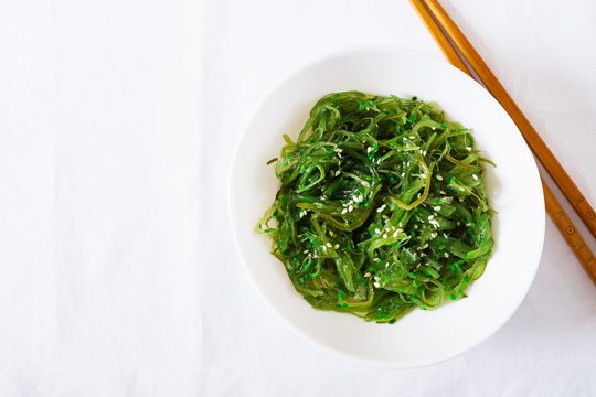 Wakame chuka or seaweed salad  with sesame seeds in bowl on white table. traditional japanese food.  top view. flat lay