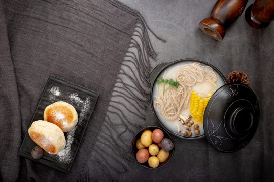 Black plate with pancakes and a bowl with noodles