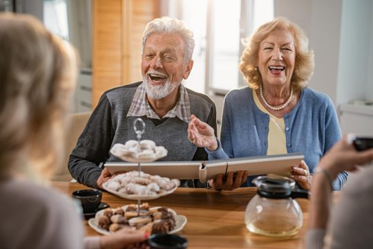 Happy senior couple having fun while communicating with their friends and looking at photo album at home