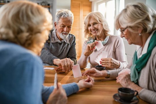 Small group of mature friends enjoying while playing cards at home