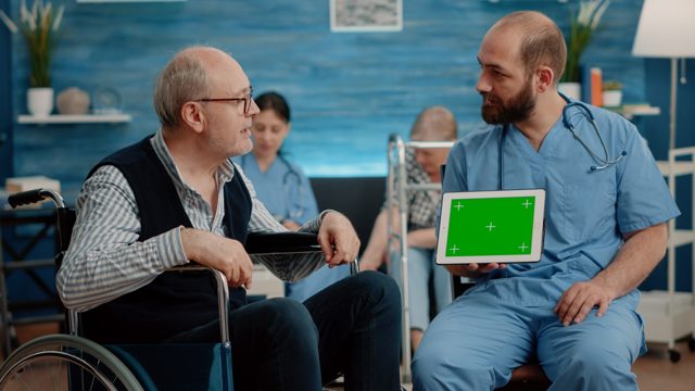 Man nurse and old patient looking at green screen on tablet