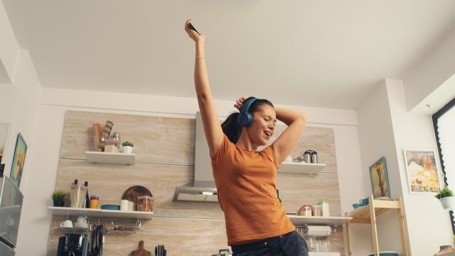 Cheerful woman singing in the kitchen in the morning. energetic, positive, happy, funny and cute housewife dancing alone in the house. entertainment and leiuse alone at home